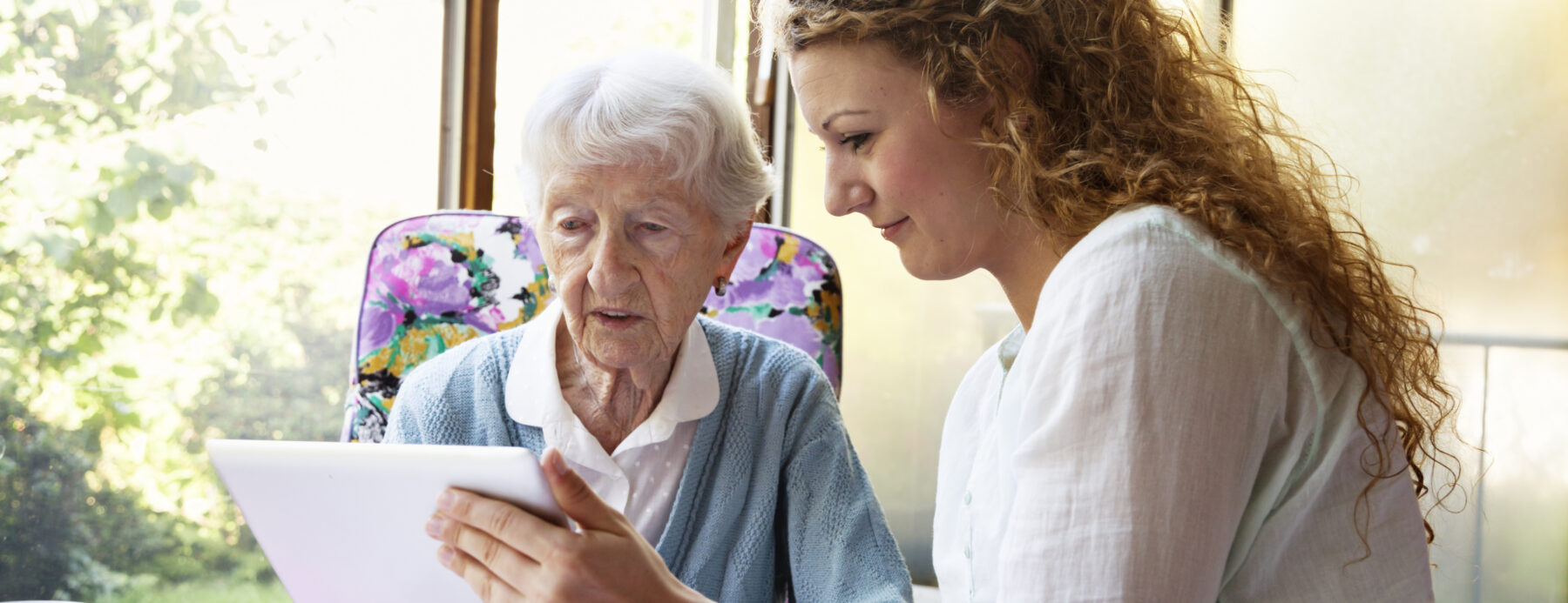 A lady holding a tablet and talking with a senior woman