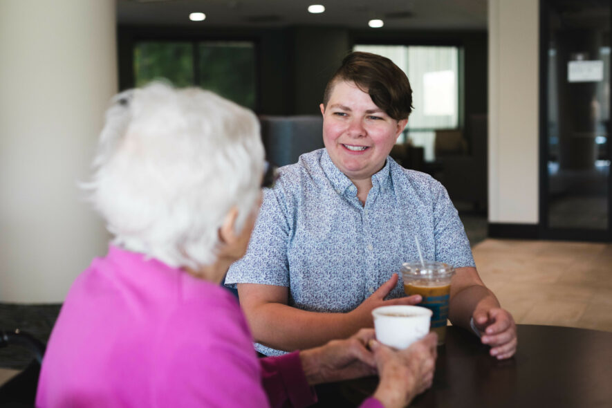 A person talking with senior woman both seated and cup of coffee in hands
